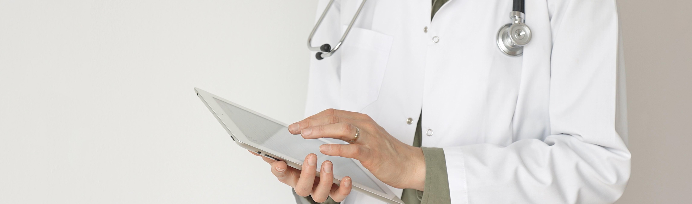 woman typing on a medical tablet wearing a white jacket and stethoscope