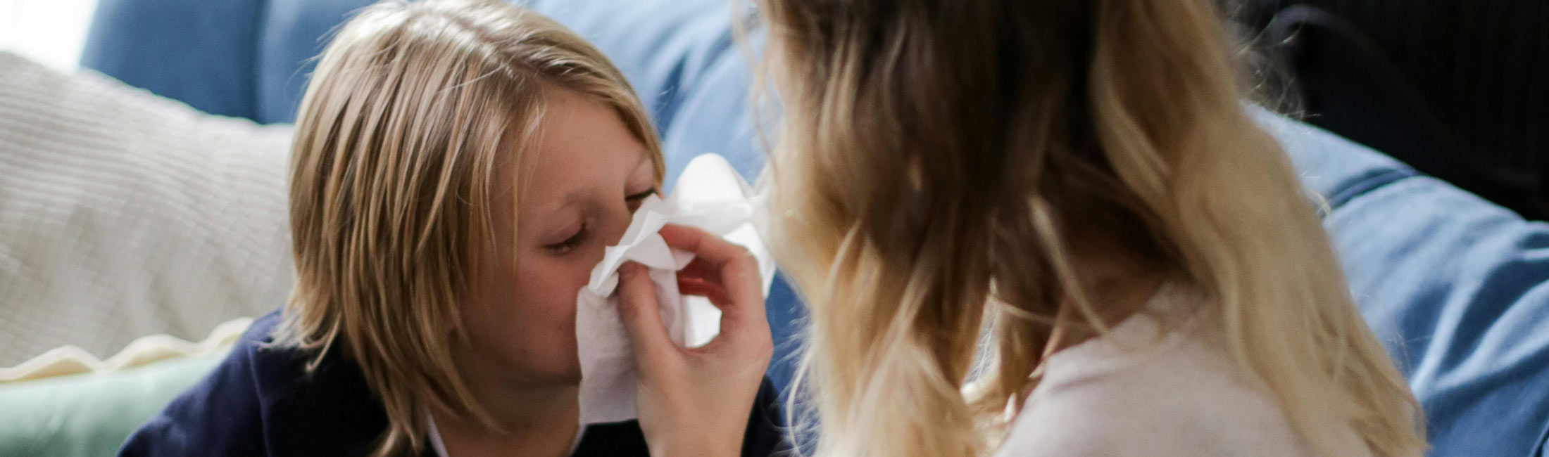 mother helping sick child blow nose