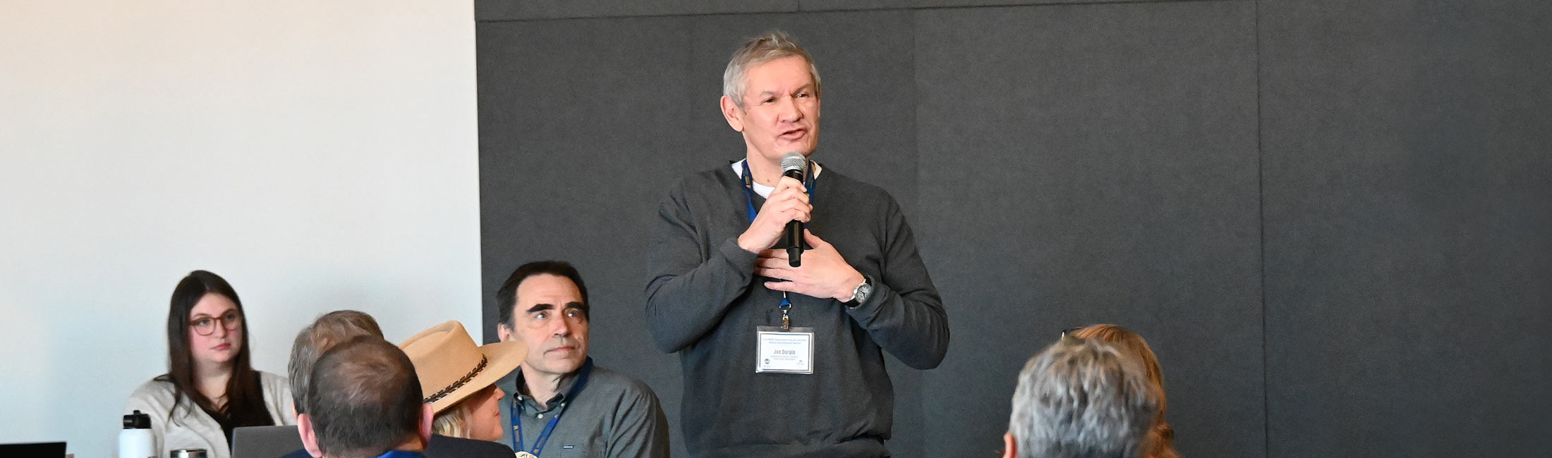 man holding microphone and speaking to people from front of meeting room