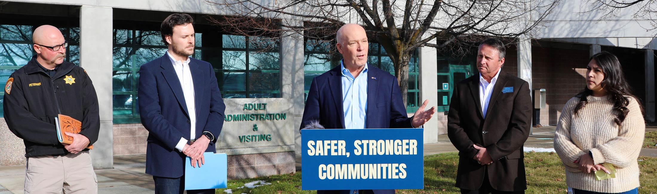 Gov. Gianforte speaking at podium behind a sign that safer, stronger communities, with four other people standing