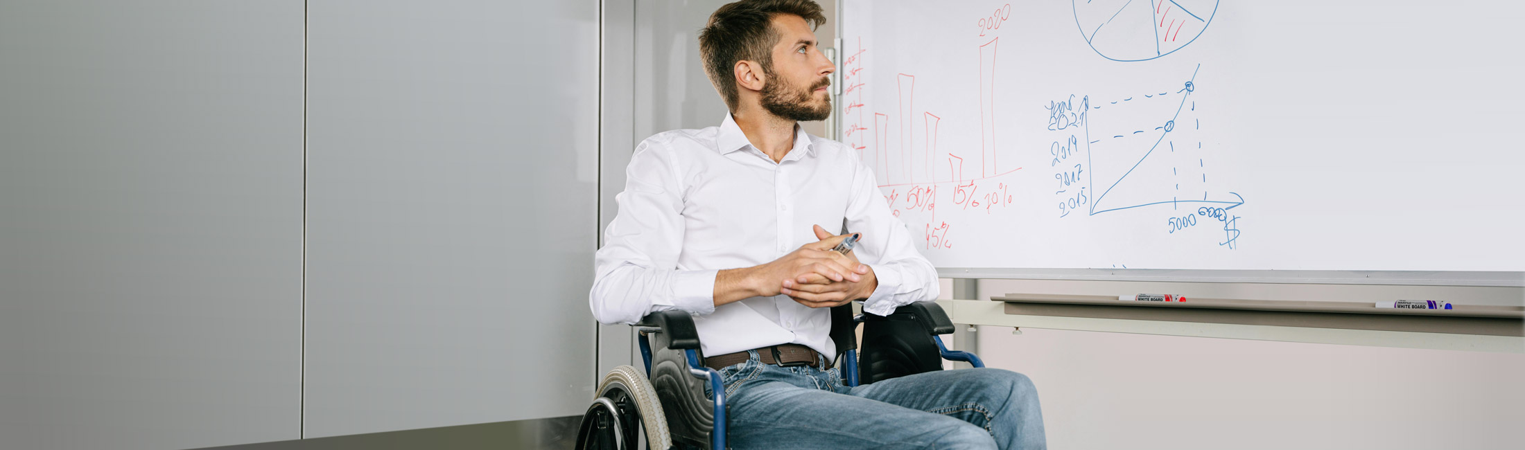 man is wheelchair looking at charts on whiteboard