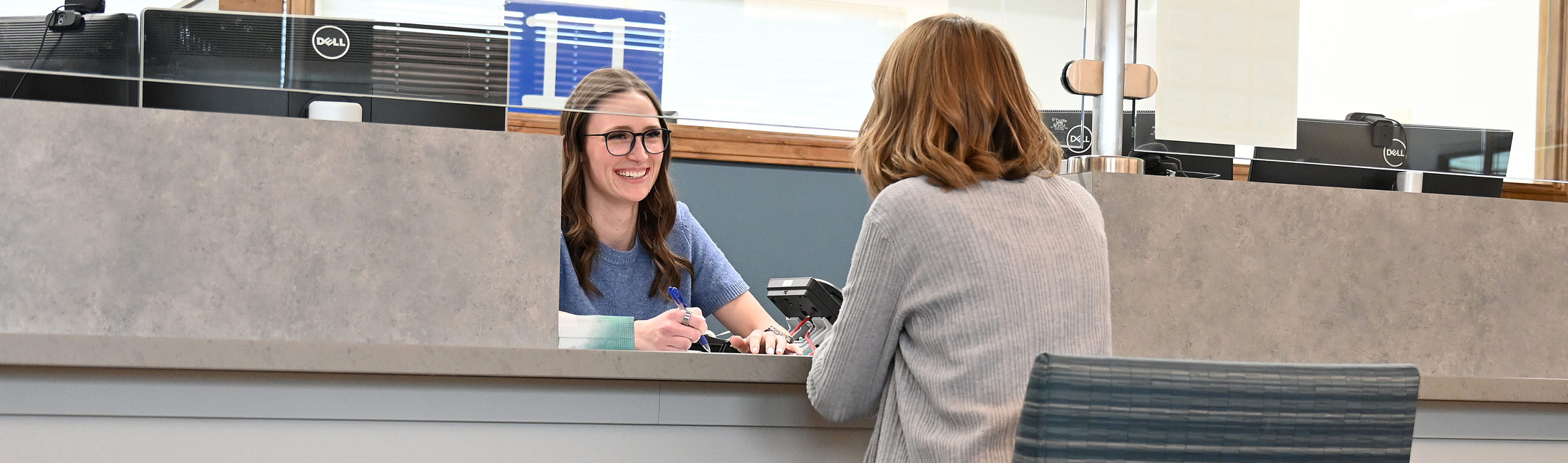 woman sitting at service desk being assisted by staff