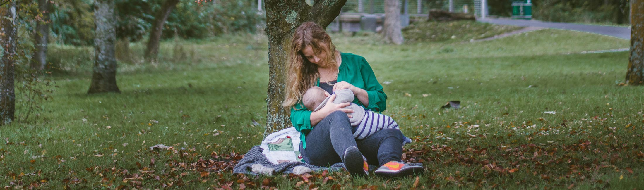 woman sitting on ground breastfeeding under a tree