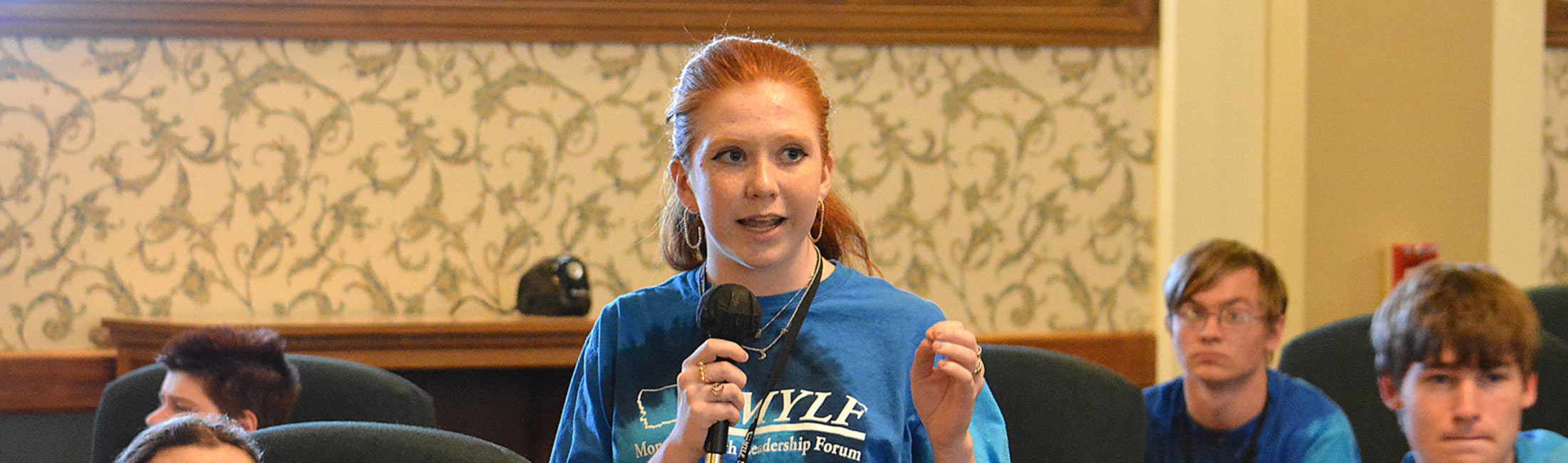 young woman speaking into microphone in front of seated peers