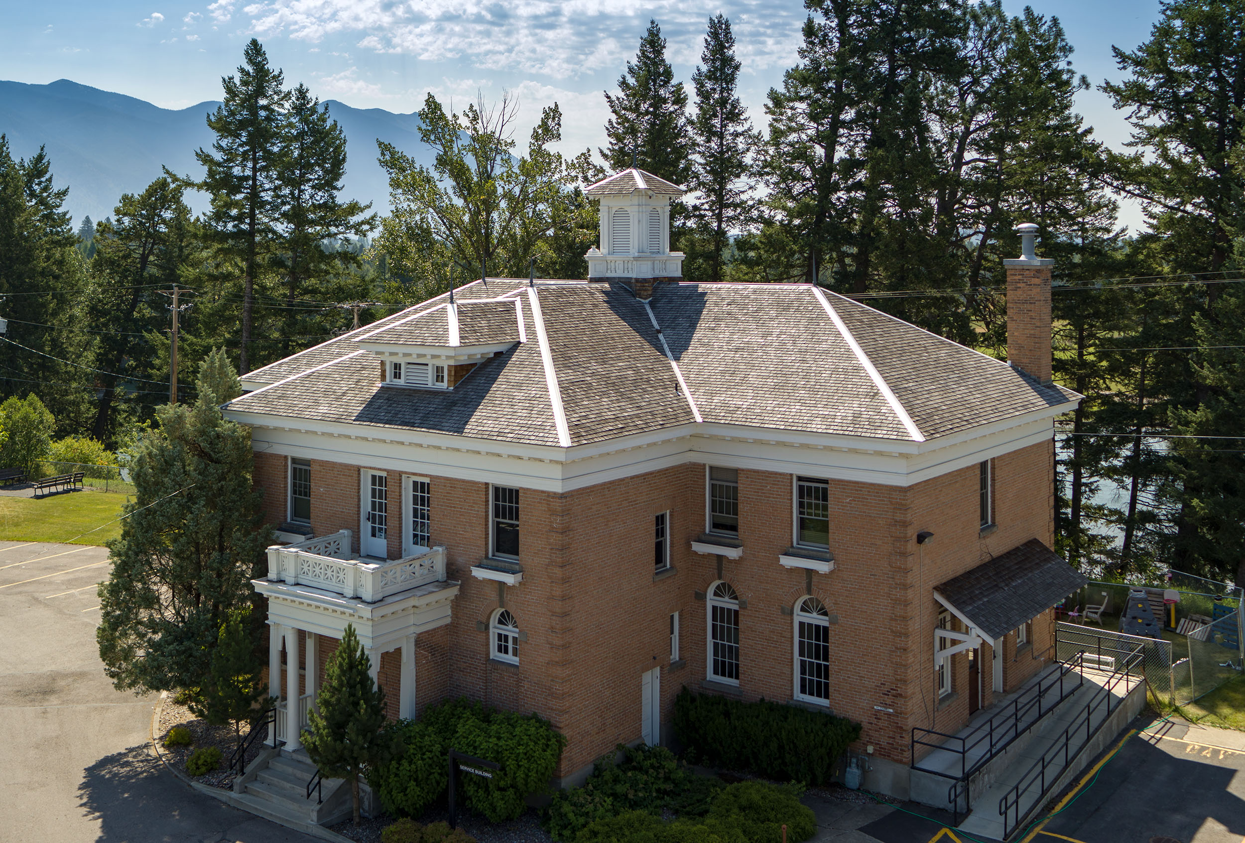 An aerial view of the main building of the Veterans Home. It is light brown brick with a slanted roof. There are pillars at the entrance door, with some trees and hedges at the front.