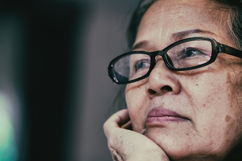 Photo of an elderly woman resting her chin in the palm of her hand, looking pensive.