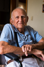 Photo of an elderly man sitting in a wheelchair, smiling at the camera