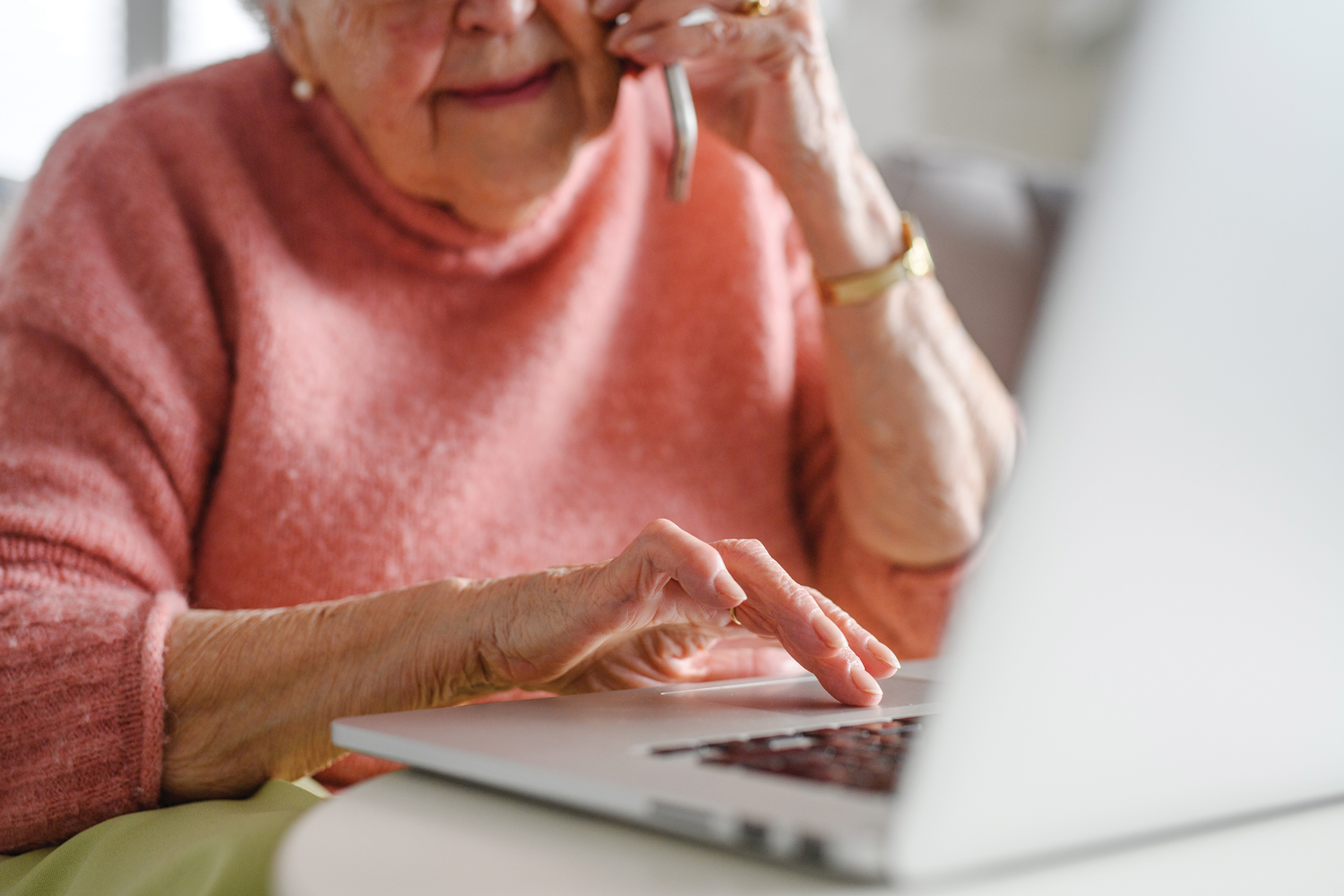 Photo of an elderly woman on the phone and typing into a laptop computer